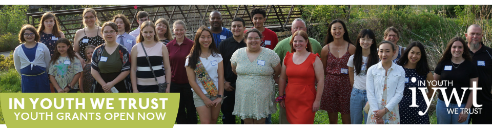 Group of people of all ages outdoors smiling at the camera. Text reads: In Youth We Trust youth grants open now
