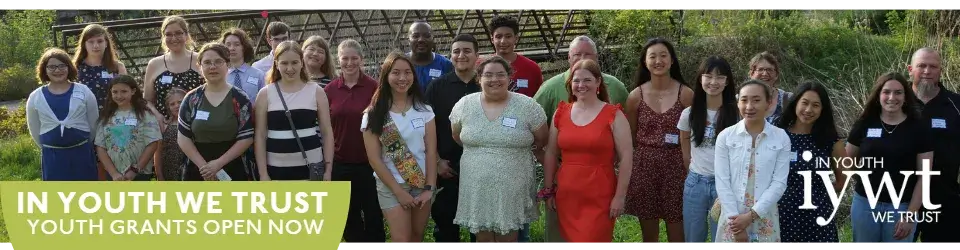Group of people of all ages outdoors smiling at the camera. Text reads: In Youth We Trust youth grants open now